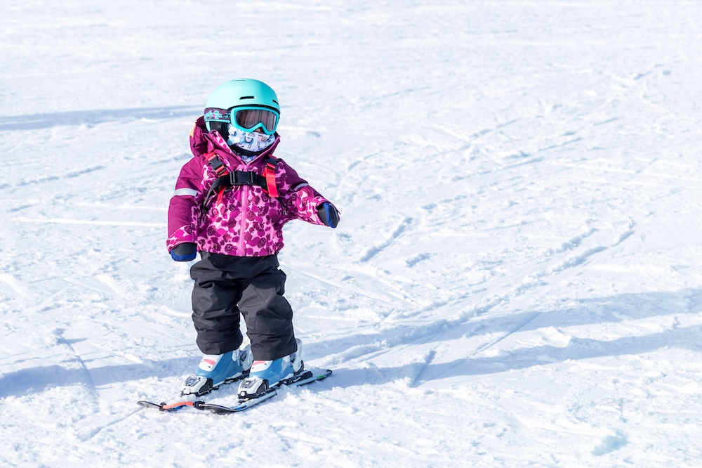 A young child in a pink ski jacket learning to ski
