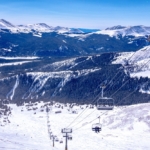Skiers ascending on the ski lift with snow-covered mountains and winter scenery in the background