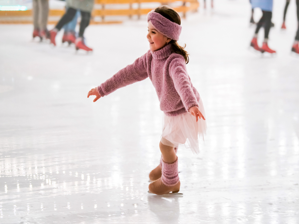 a girl in a pink turtleneck sweater, tutu, headbank and legwarmers skates on an ice rink, a popular winter activity in breckenridge